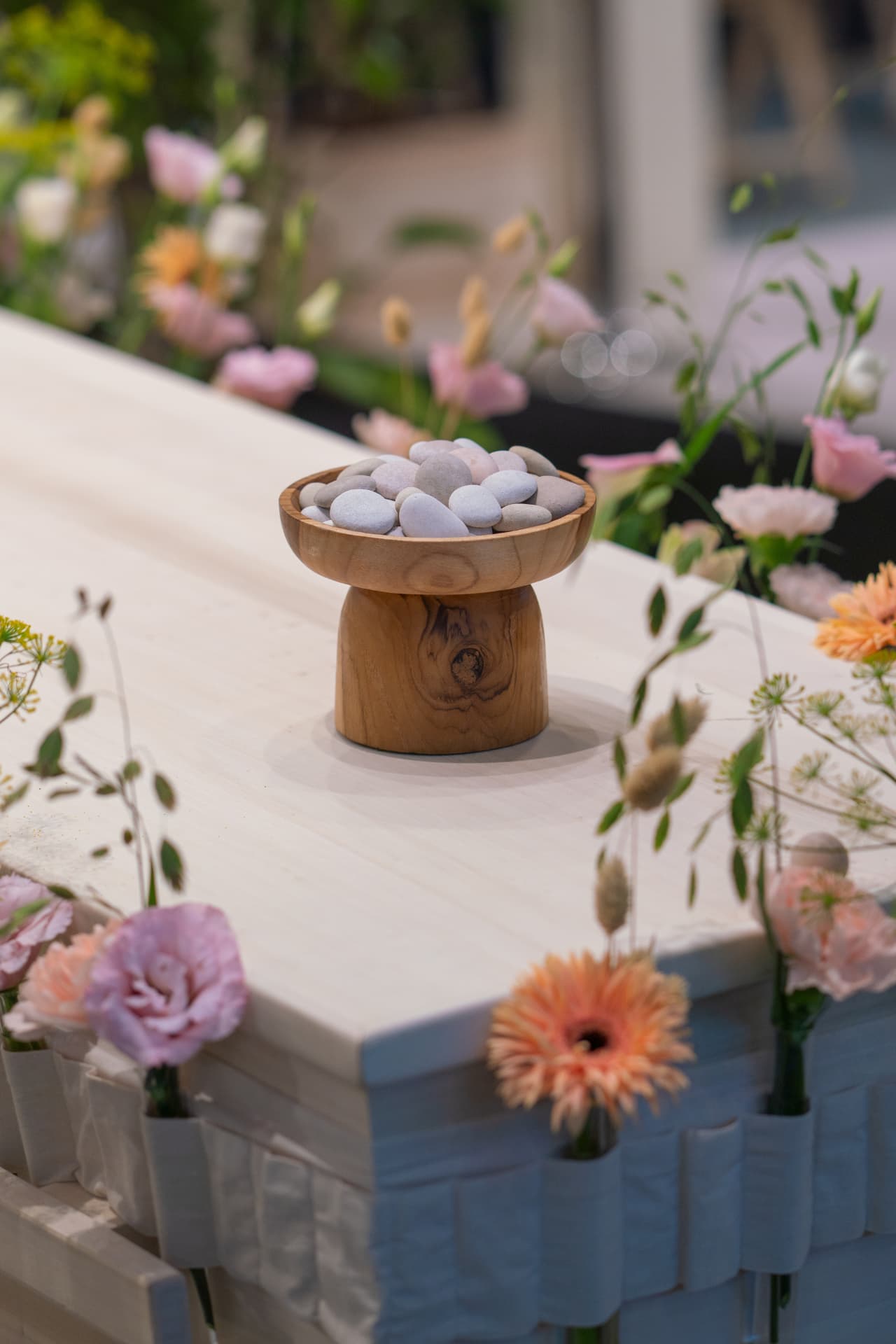 Een houten voetstukje met steentjes tussen bloemen